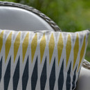 Close-up of a cushion with yellow, white and grey geometric pattern on a chair outdoors.