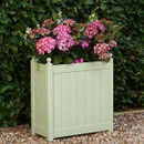Sage green square garden planter filled with pink hydrangeas, set on gravel in front of a leafy hedge.