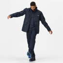 A man in a navy jacket and pants steps forward with one foot raised, exuding confidence. The outfit is casual, complemented by bright blue-soled shoes.