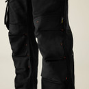 Detail: Close-up of reinforced knee panels on black work trousers, durable fabric with Cordura tag, heavy-duty stitching for industrial workwear.