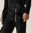 Angled view: Men’s black utility work trousers with holster pockets carrying screwdriver, heavy-duty cargo pants with functional tool loops, industrial workwear design.