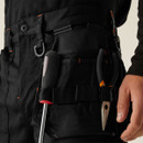 Close-up: Black work trousers tool holster pocket holding screwdriver and pliers, durable utility pants with reinforced fabric, tradesman workwear detail, secure tool storage.