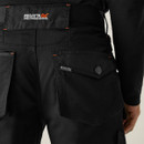 Detail: Close-up of back pocket with button flap on black work trousers, Regatta Professional logo label, durable utility design.