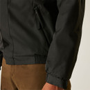A close-up of a person wearing a black jacket and brown pants. The focus is on the jacket's waist and arm area, showing a zippered pocket.