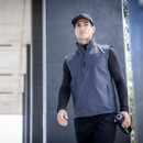 Man walking outdoors wearing navy softshell vest, black cap and athletic wear, modern lightweight workwear gilet with zip pockets