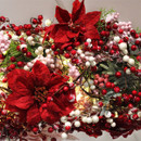 Festive arrangement featuring bright red poinsettias, red and white berries, and green foliage. The decorations convey a vibrant, celebratory holiday tone.