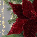 Close-up of a glittery red poinsettia next to green pine needles, with warm, blurred lights in the background, evoking a festive holiday feel. Close-up of a glittery red poinsettia next to green pine needles, with warm, blurred lights in the background, evoking a festive holiday feel.