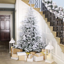Snow-flocked artificial Christmas tree displayed in a hallway with wrapped presents and lanterns, creating a classic winter wonderland festive centrepiece.