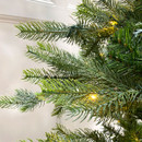 Close-up of artificial Christmas tree branches with warm white LED lights woven through realistic green pine needles for a natural festive appearance.