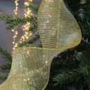 Close-up of a shimmering gold ribbon entwined around a green Christmas tree branch, with soft, glowing fairy lights in the background. Festive and elegant.