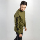 A man in an olive green long-sleeve shirt with "Caterpillar" printed on the sleeve looks down to his left. He wears black jeans, set against a plain light background. The tone is casual and contemplative. A man in an olive green long-sleeve shirt with "Caterpillar" printed on the sleeve looks down to his left. He wears black jeans, set against a plain light background. The tone is casual and contemplative.