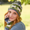 A young woman with red hair smiles warmly, wearing a colourful knitted hat and fingerless gloves featuring sheep patterns. She's outdoors, conveying a cosy, cheerful vibe.
