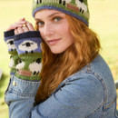 A person with long red hair wearing a denim jacket smiles softly. They sport a knitted hat and fingerless gloves with sheep patterns, conveying a cosy and warm vibe.