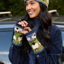 Smiling woman wearing a blue and green knit hat and fingerless gloves with a sheep pattern. She stands by a car, exuding warmth and joy.