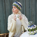 A woman in a cream jumper and knit sheep headband holds a floral mug. A matching teapot with a cosy sits nearby. The mood is cosy and relaxed. A woman in a cream jumper and knit sheep headband holds a floral mug. A matching teapot with a cosy sits nearby. The mood is cosy and relaxed.