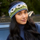 A woman wearing a colourful knit headband with sheep patterns, set against a blurred natural background. She has long, dark hair and a slight smile. A woman wearing a colourful knit headband with sheep patterns, set against a blurred natural background. She has long, dark hair and a slight smile.