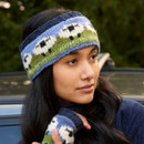 Woman wearing a blue and green knitted headband and fingerless gloves with sheep patterns. She gazes thoughtfully, with greenery in the background. Woman wearing a blue and green knitted headband and fingerless gloves with sheep patterns. She gazes thoughtfully, with greenery in the background.