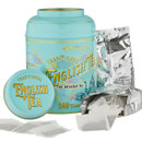 A turquoise tin labelled "Traditional English Tea" with floral designs, surrounded by loose tea bags and an open foil package. Classic and inviting.