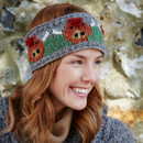 Smiling woman with red hair wears a knitted headband featuring orange flowers against a stone wall. Her cosy jumper adds to the cheerful, autumnal feel. Smiling woman with red hair wears a knitted headband featuring orange flowers against a stone wall. Her cosy jumper adds to the cheerful, autumnal feel.