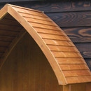 Close-up of the arbour’s curved, slatted stained wood roof against a dark wooden wall.