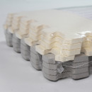 Detailed image of interlocking floor mats stacked together, showing white and grey foam pieces with textured surface for non-slip grip and easy assembly.