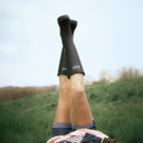 Lifestyle image of black Barbour wellington boots worn outdoors, legs raised against a grassy countryside backdrop.