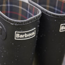 Close-up of Barbour logo badge on black rubber wellington boots with water droplets on the surface.