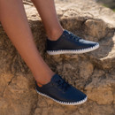 Navy leather lace-up shoes with white whipstitched sole shown on a model sitting on rocky steps outdoors.