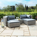 Two cushioned, grey wicker patio chairs with a small matching table on a stone patio, surrounded by lush greenery and under a bright blue sky.