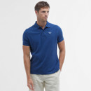 Man wearing a blue polo shirt and beige pants, looking to the side against a plain white background. The atmosphere is casual and relaxed.