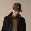 A person in a brown cap and scarf, wearing a black jacket over a brown jumper, looking down. The mood appears calm and introspective.