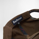 Close-up of a brown Barbour cap featuring a visible inner label with the logo in white on blue. The interior shows a subtle plaid lining.