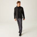 A man wearing a black jacket and gray pants walks confidently in a minimalist, light-coloured space. The tone is casual and sporty. A man wearing a black jacket and gray pants walks confidently in a minimalist, light-coloured space. The tone is casual and sporty.