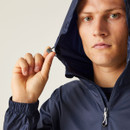A person wearing a navy windbreaker holds the hood's drawstring, looking serious. The background is neutral, emphasizing the jacket's casual style.