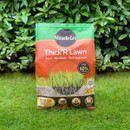 Bag of Miracle-Gro Thick'R Lawn seed and fertilizer on lush grass, set against dense green foliage. The packaging is red and green, emphasizing growth.