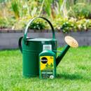 Green watering can and Miracle-Gro Fast Green lawn food placed on vibrant grass with blurred garden plants as background, suggesting gardening activity.