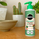 A bottle of Miracle-Gro Organic Pump & Feed plant food on a wooden surface, surrounded by potted cacti and a ceramic bowl, conveying a natural, nurturing vibe.