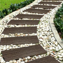 Curved garden path with dark wooden planks set in light pebbles, bordered by greenery. The serene setting suggests tranquility and natural beauty.