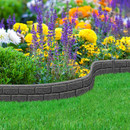 A vibrant garden with a curved stone border features blooming purple lavender, yellow marigolds, and green shrubs, set against a lush green lawn.