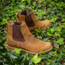 Brown leather Chelsea boots with dark elastic panels are placed on lush green ivy leaves, conveying a rustic and outdoor aesthetic.