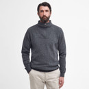 A bearded man in a grey quarter-zip jumper and light khaki pants stands against a plain white background, exuding a calm and relaxed demeanour.