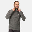 A man smiles while adjusting the collar of a grey zip-up sweater with a logo. He stands against a plain white background, conveying a casual and relaxed vibe.