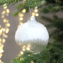 A clear glass bauble with a snow effect covering the top half, hanging from a Christmas tree.