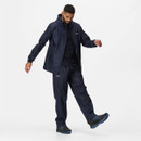 Man in navy waterproof jacket and trousers with hood, stepping forward. His focused expression suggests activity or exploration. White background.