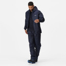 A man wearing a navy waterproof jacket and trousers walks confidently against a plain white background. He appears casual and ready for outdoor activities.