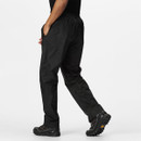 Person in black athletic trousers and trail shoes walking, with one hand in pocket. The background is plain white, conveying a sense of movement and style.