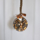 A glass ball LED rope light with warm white lights, hung against a white wooden background.
