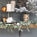 Faux eucalyptus garland draped across a festive mantel shelf, featuring frosted green leaves and soft white berry accents alongside seasonal Christmas decorations.