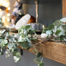 Artificial eucalyptus foliage garland cascading over a rustic wooden mantel, adding natural greenery to festive home decorations.
