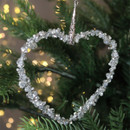 A close up view of a silver beaded heart decoration hanging from a Christmas tree.